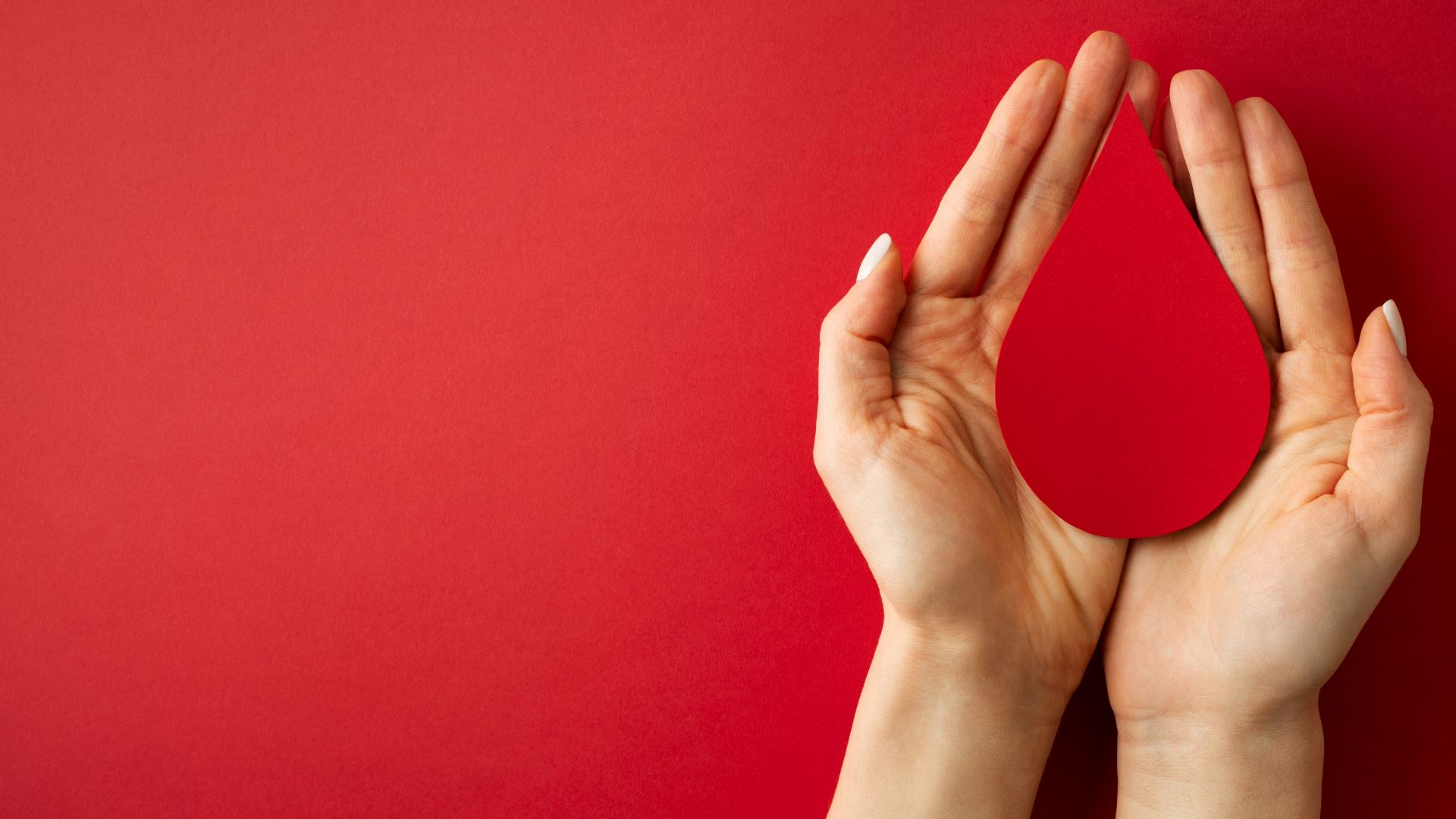 Hands holding a red droplet in front of a red background.