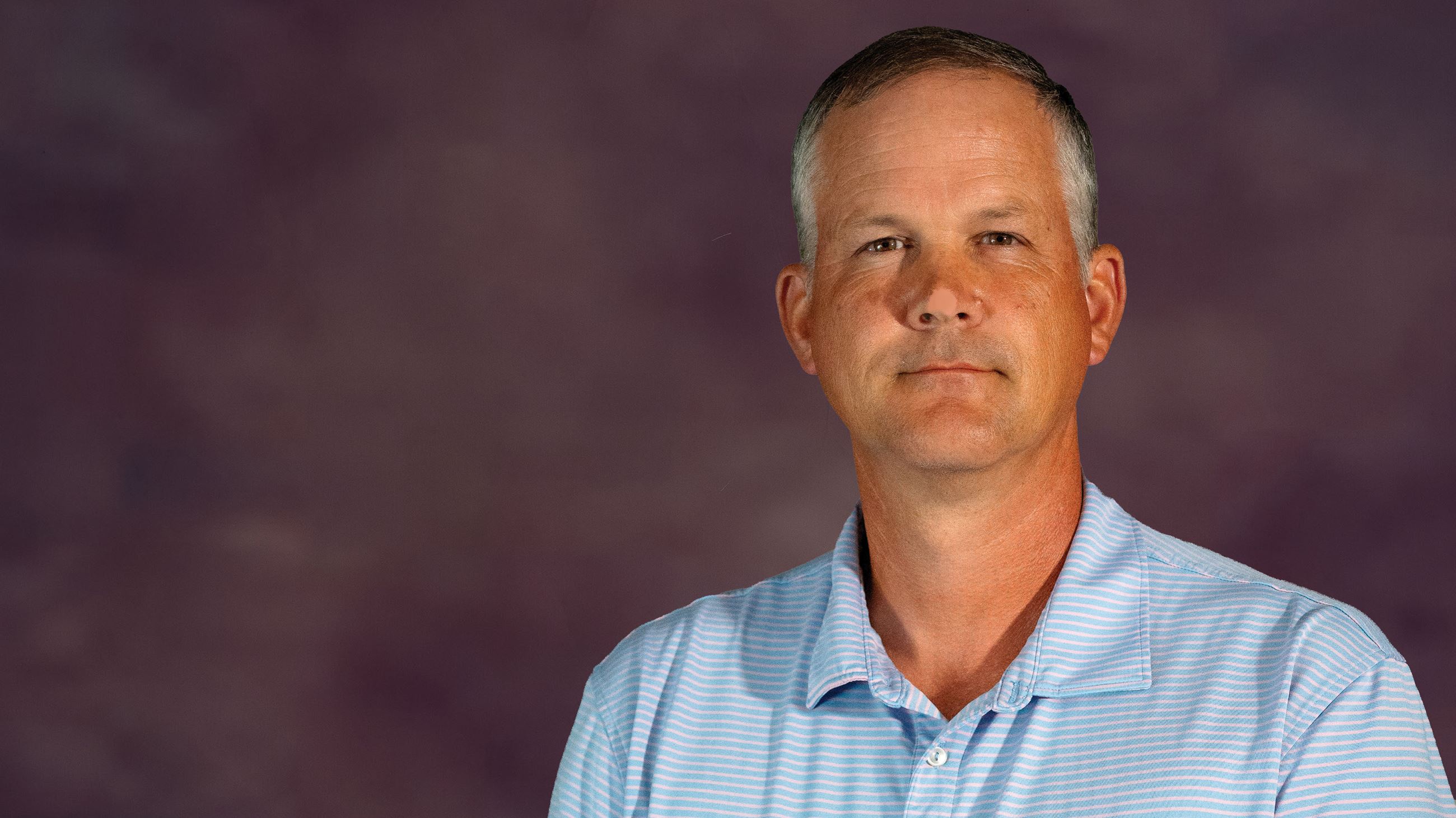 Man in a blue polo smiles in front of a purple background