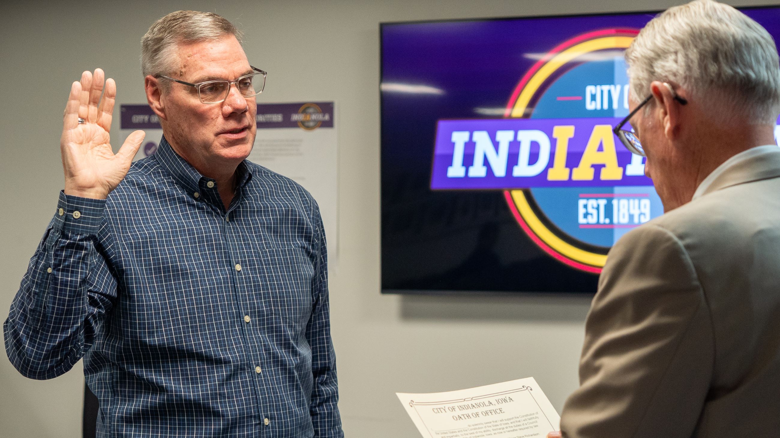 A man wearing glasses and a blue button down shirt raises his right arm and repeats a statement.