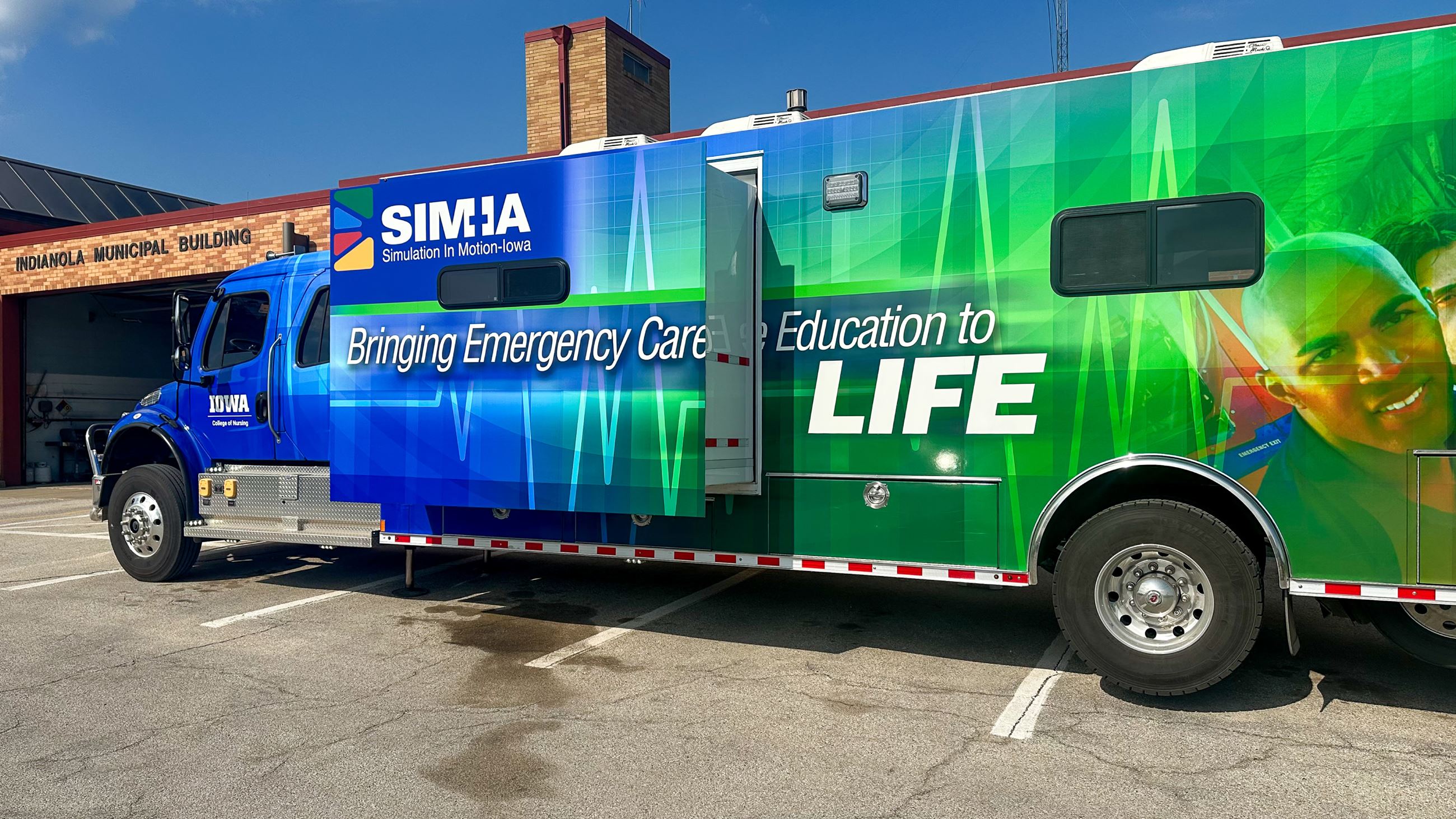 a large blue and green vehicle in the parking lot outside Indianola Fire Station.