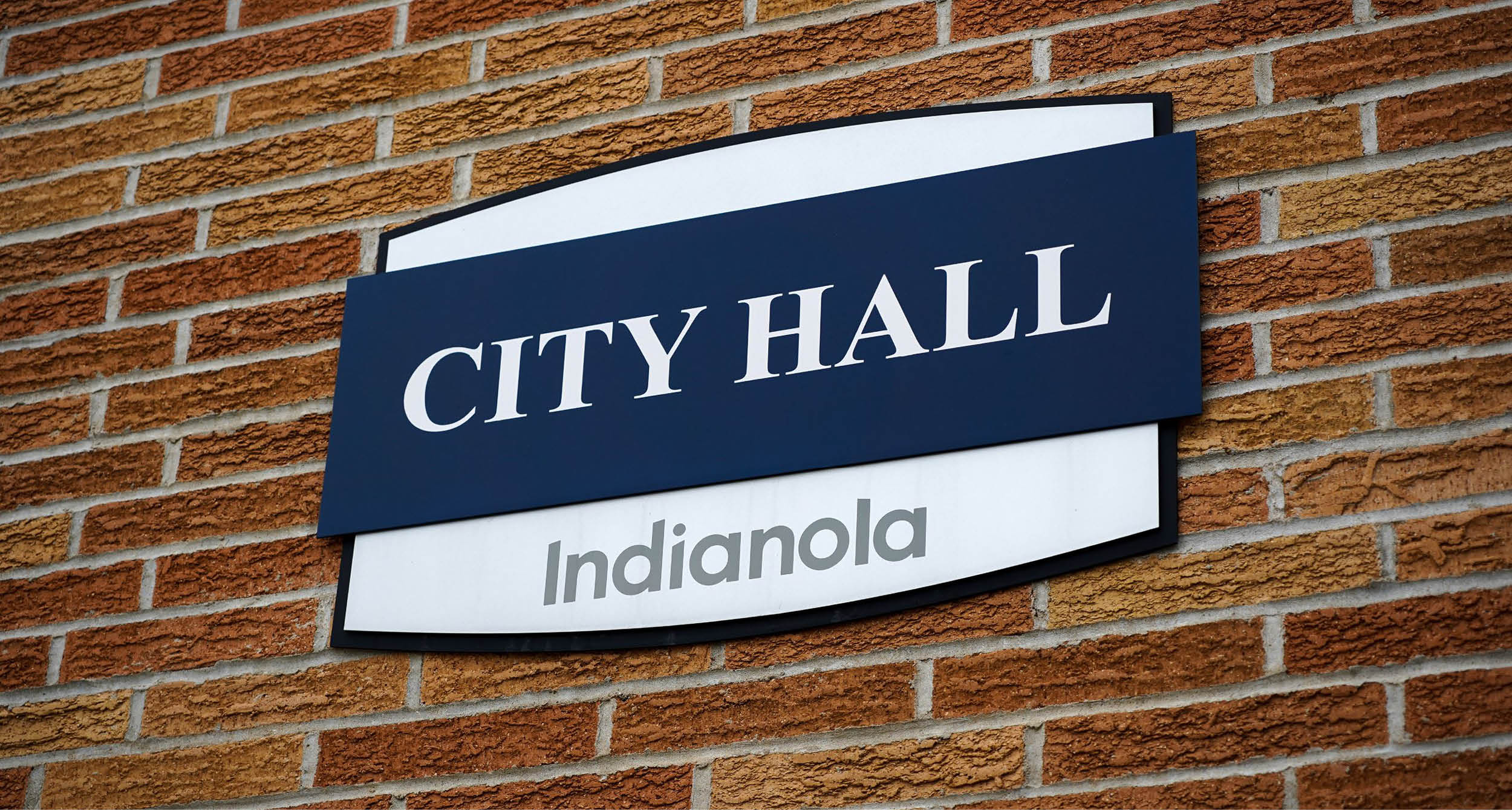 A navy and blue sign on a brick wall that says Indianola City Hall.