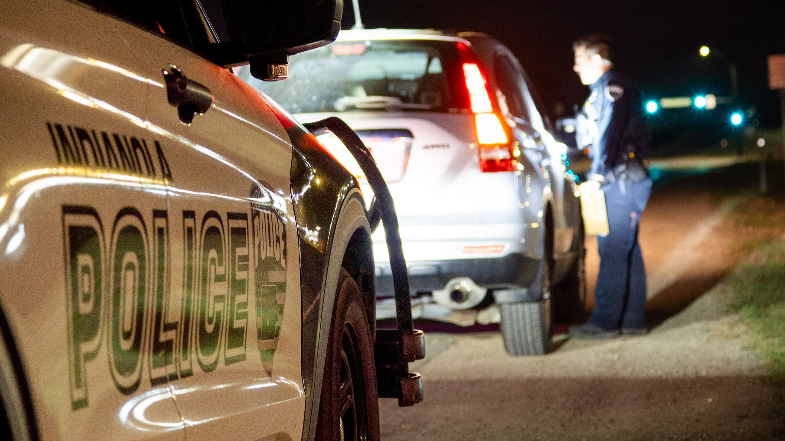A police officer pulls over a vehicle in front of a traffic light at night.