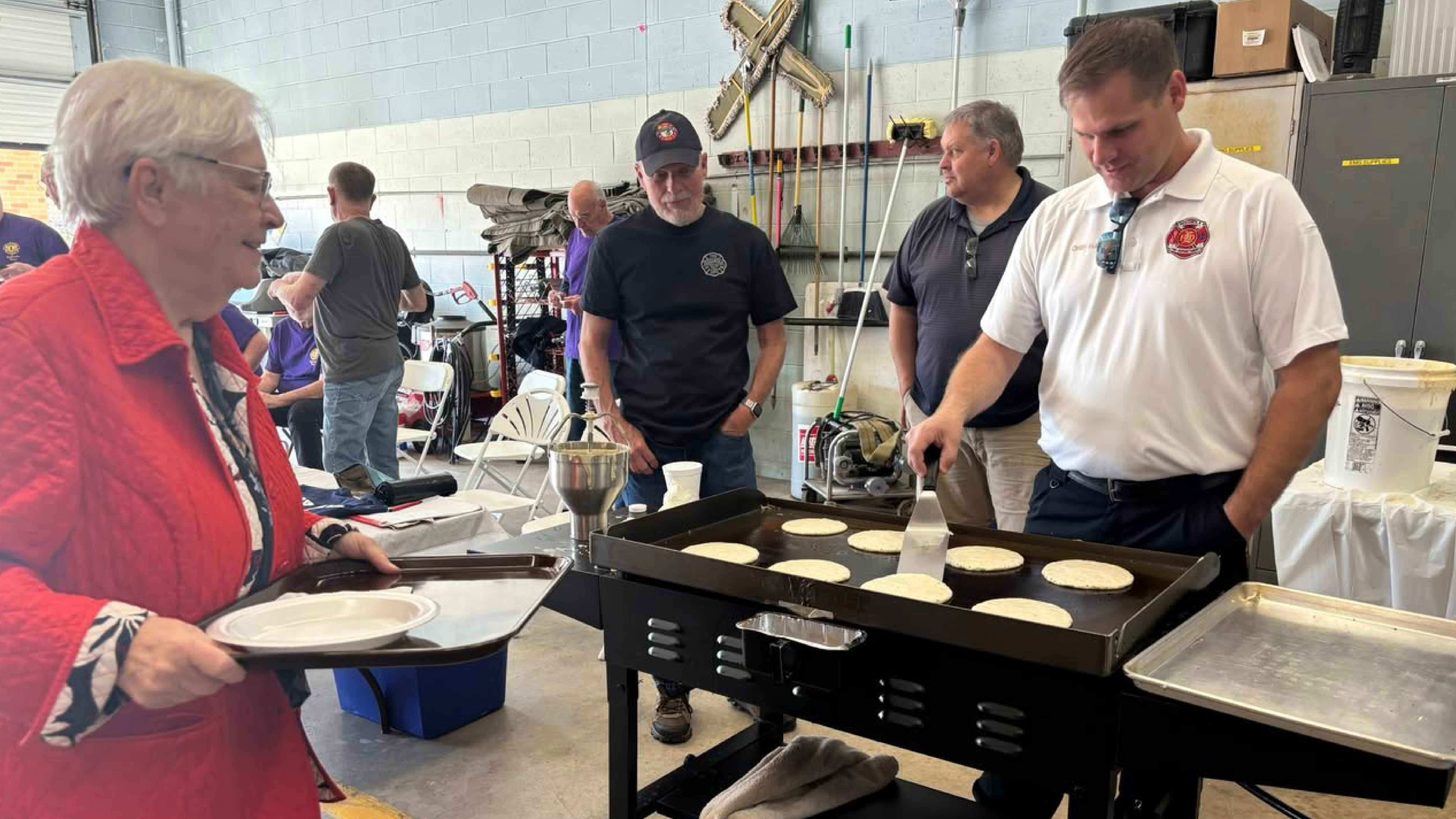 A group of men making pancakes and serving them to a woman waiting in line.