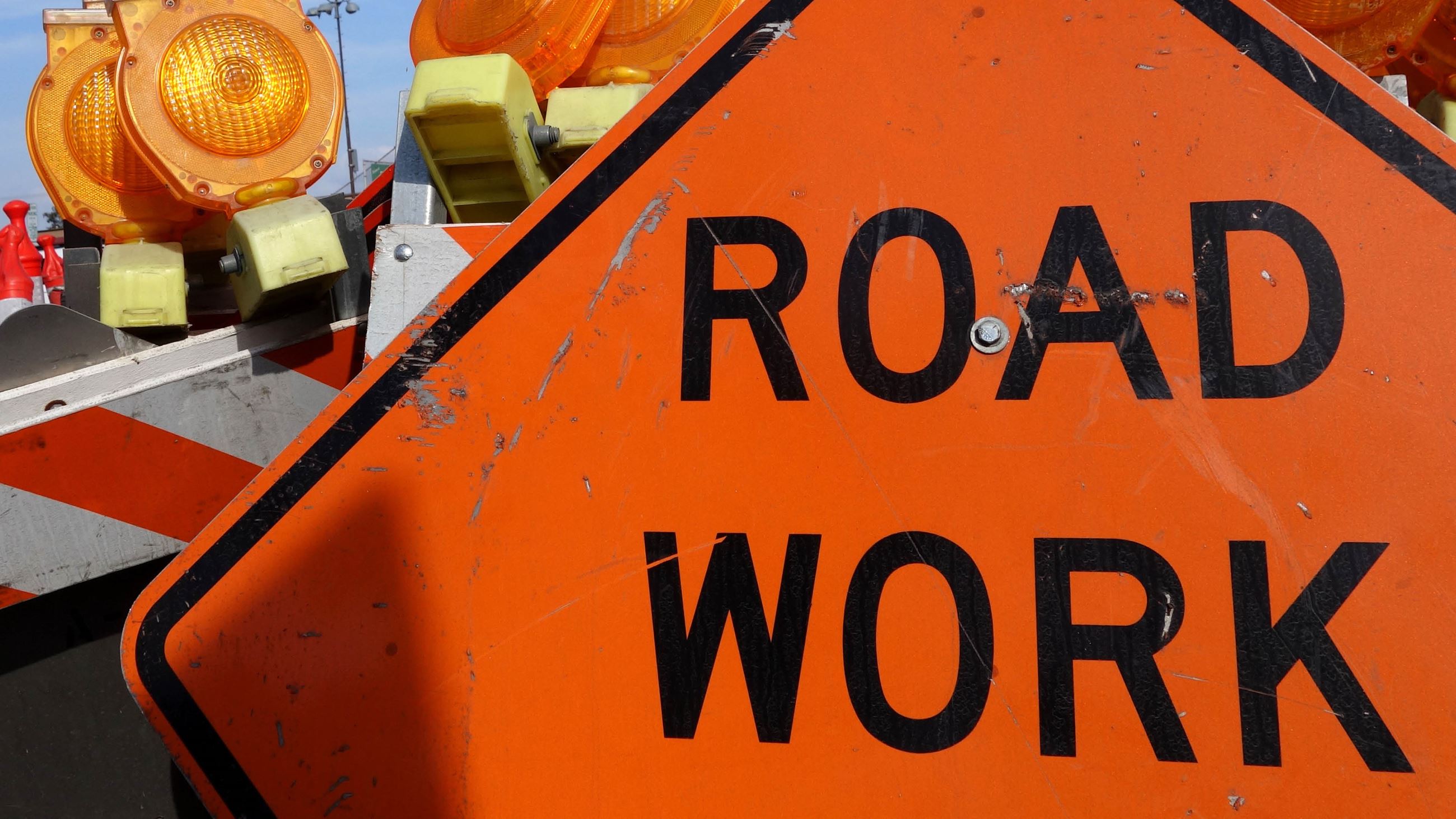 An orange road work sign standing next to barricades in a street.