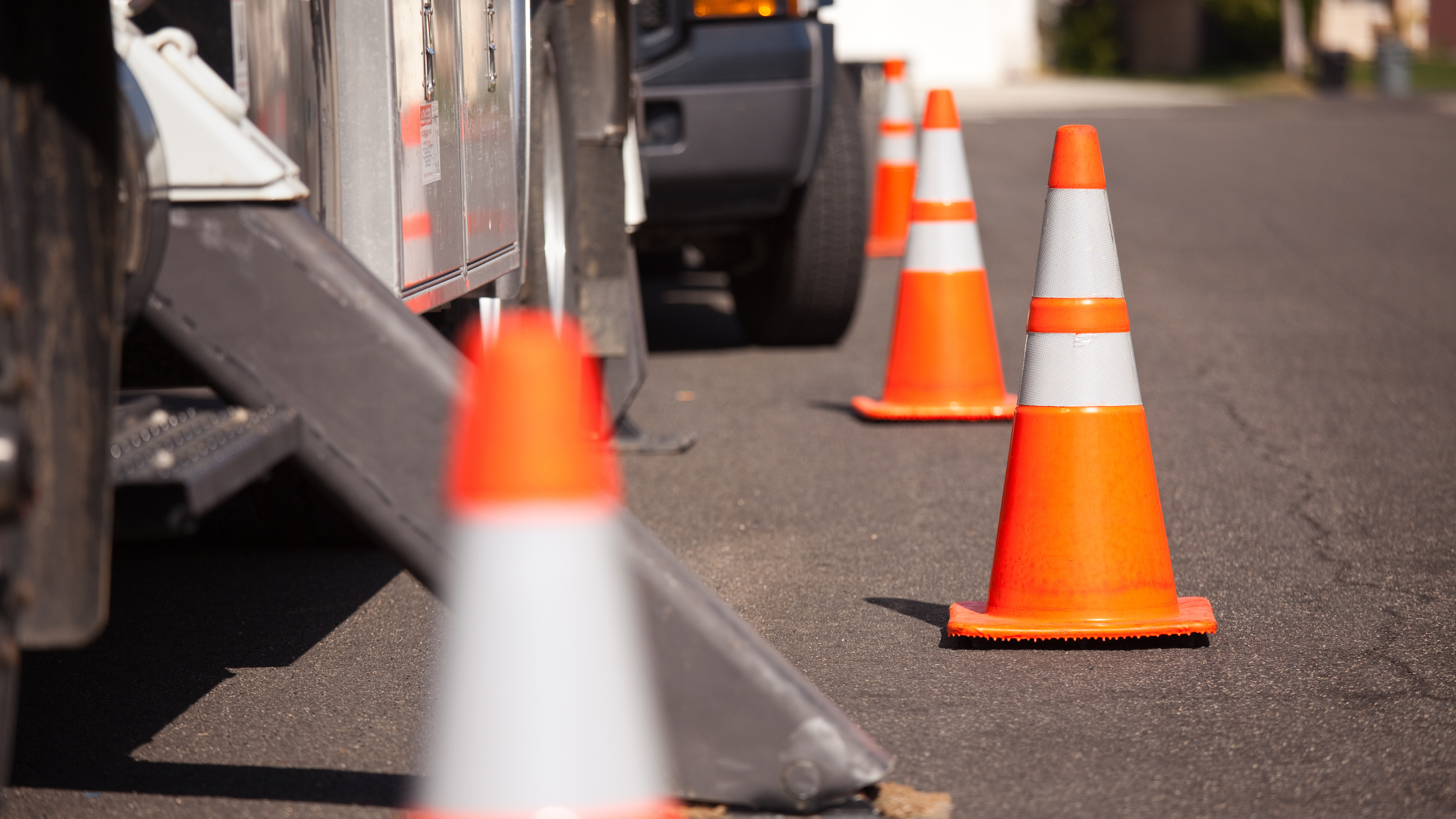 Orange and white pylons along a roadway with work trucks