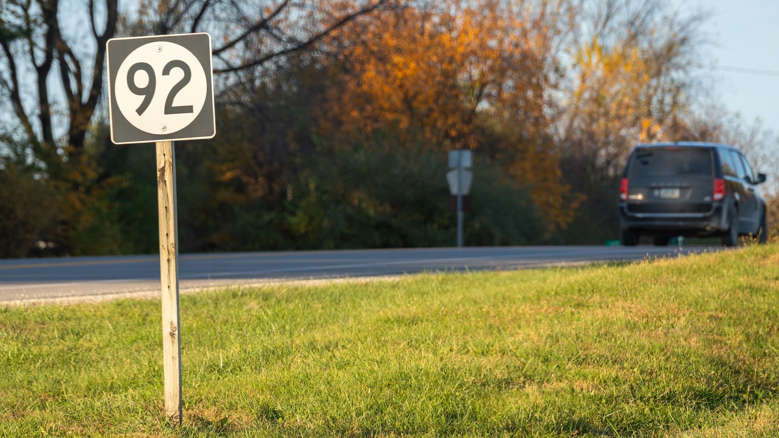 A Highway 92 road sign stands along a roadway with a vehicle passing.