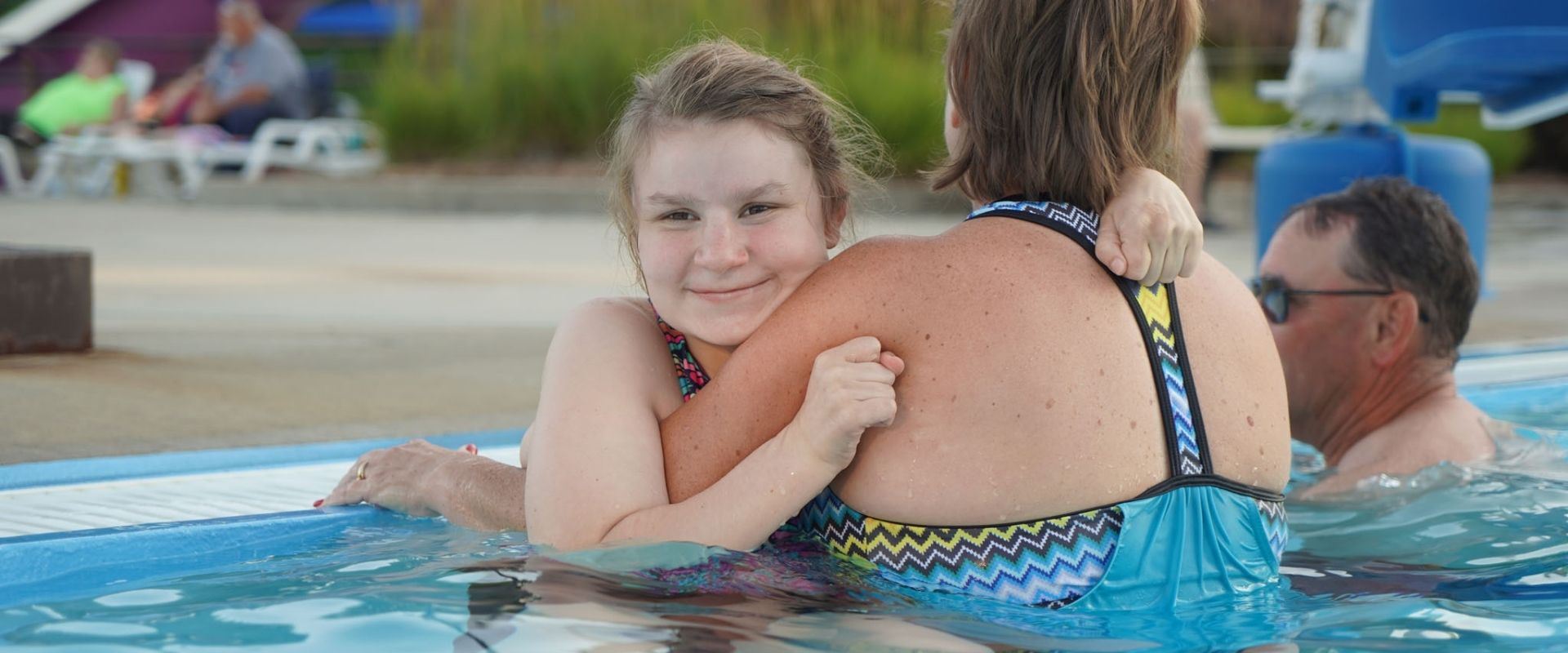 A young girl hangs on to her mother in the pool