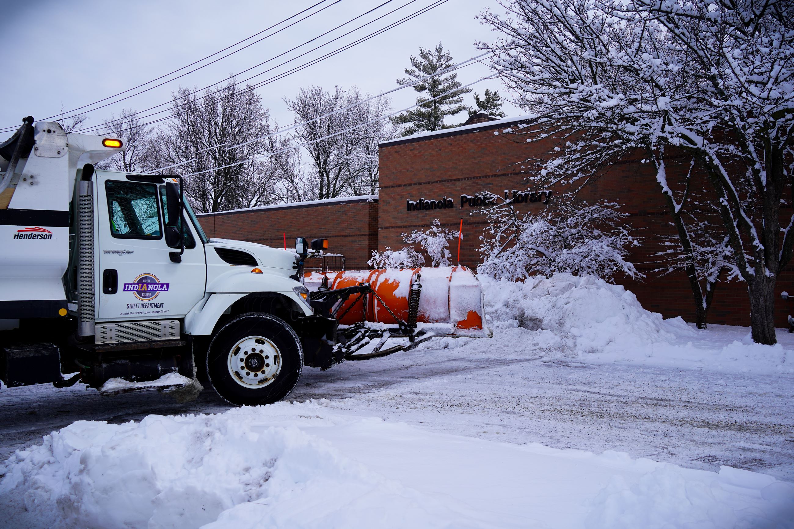 An Indianola Streets Department Snow Plow is removing snow near the Indianola Public Library
