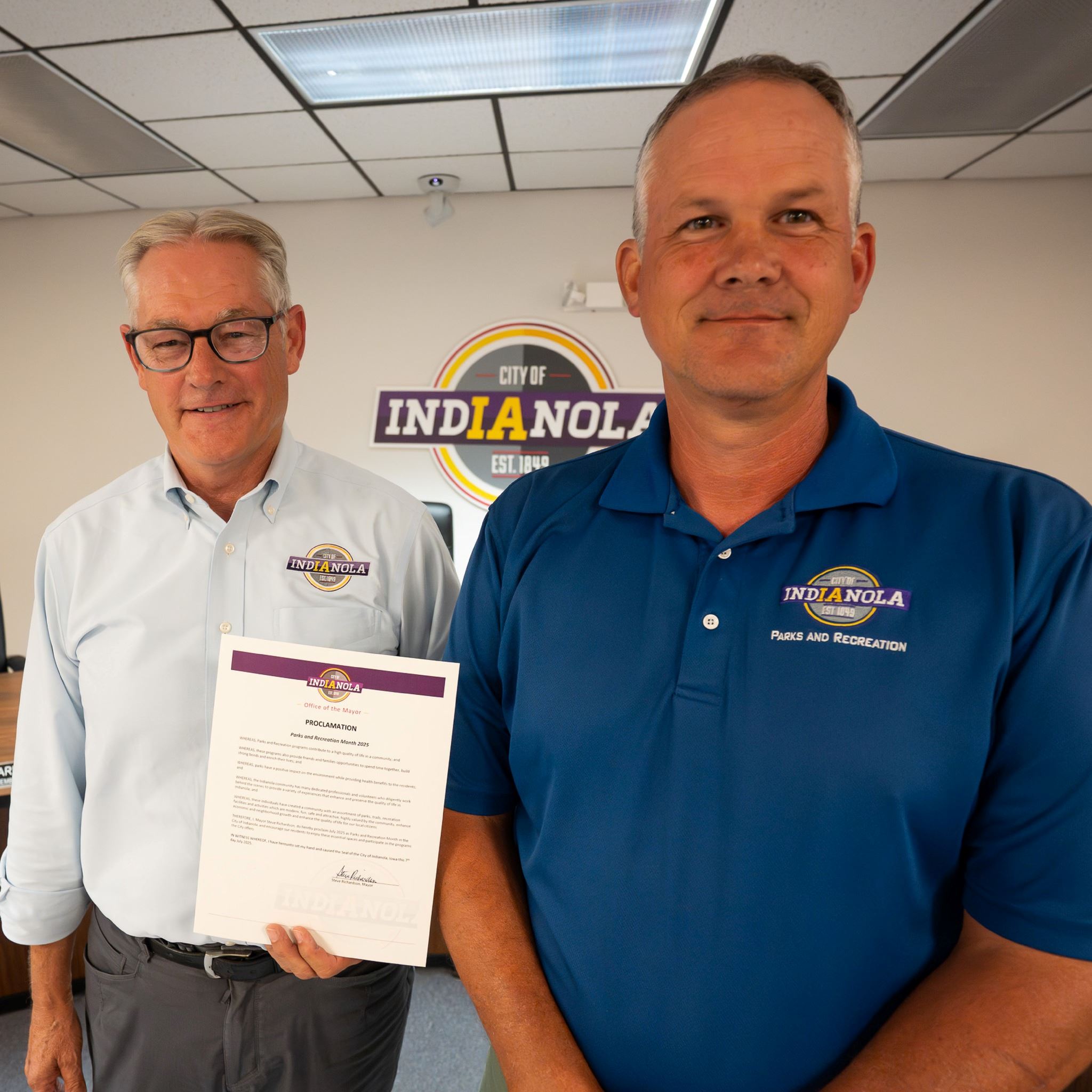 Two men pose for a photo holding a proclamation announcing Parks & Rec Month in Indianola.