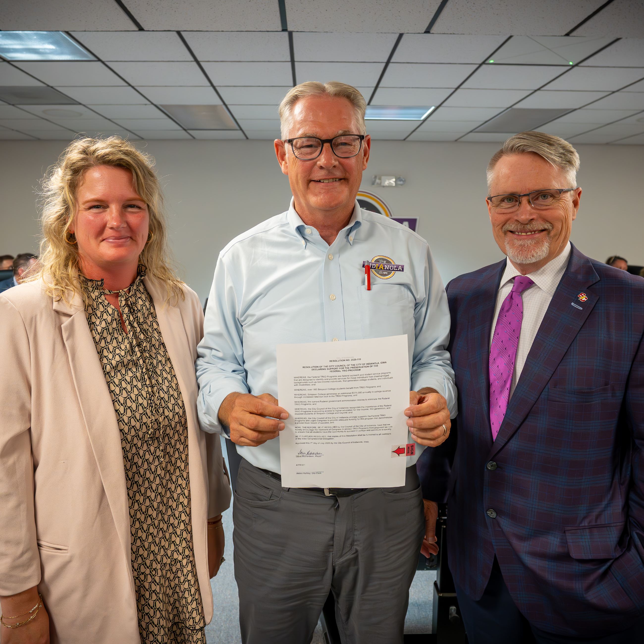 A woman and two men pose for a photo holding a signed resolution at the City Council meeting.