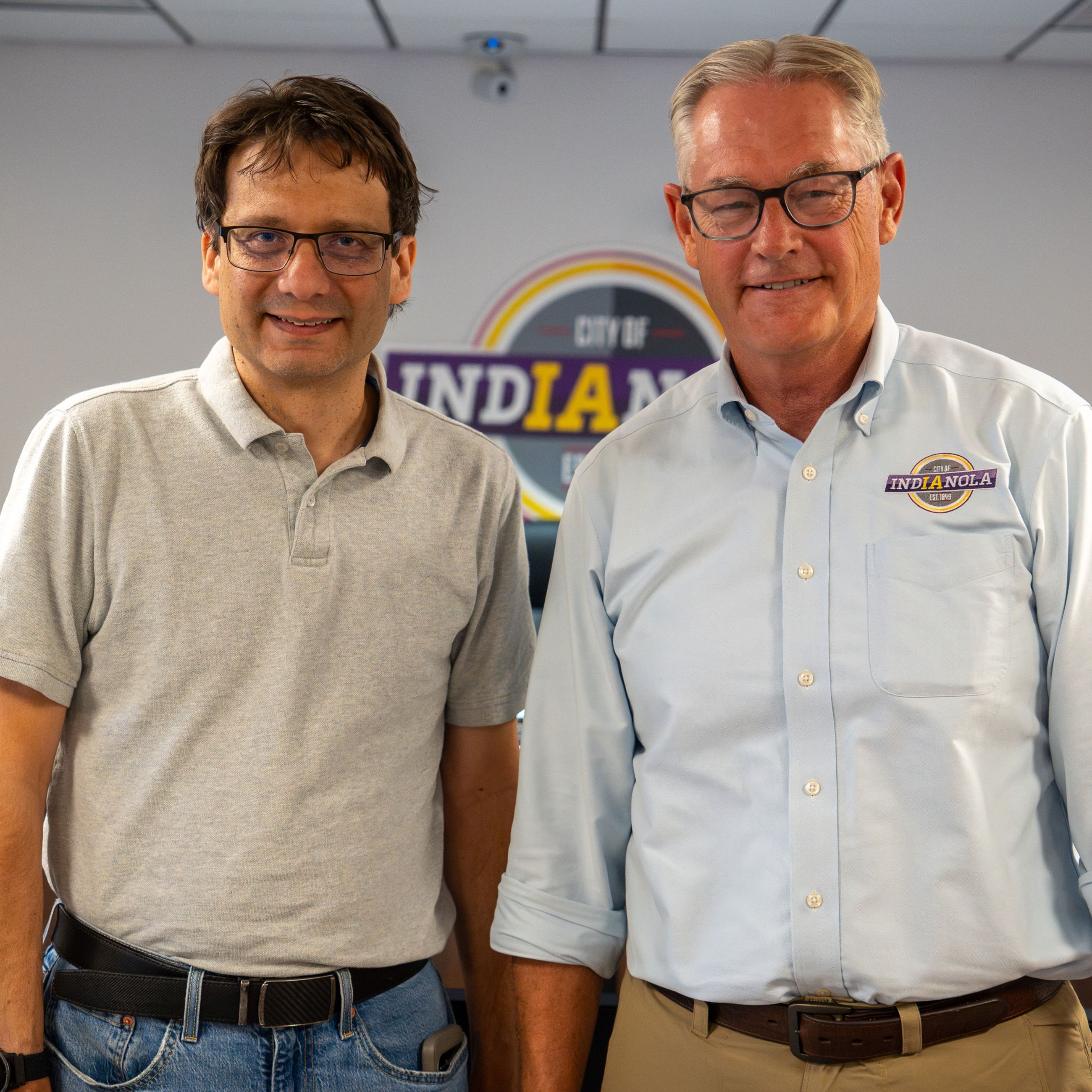 Two men pose for a photo standing inside the Council Chambers at Indianola City Hall