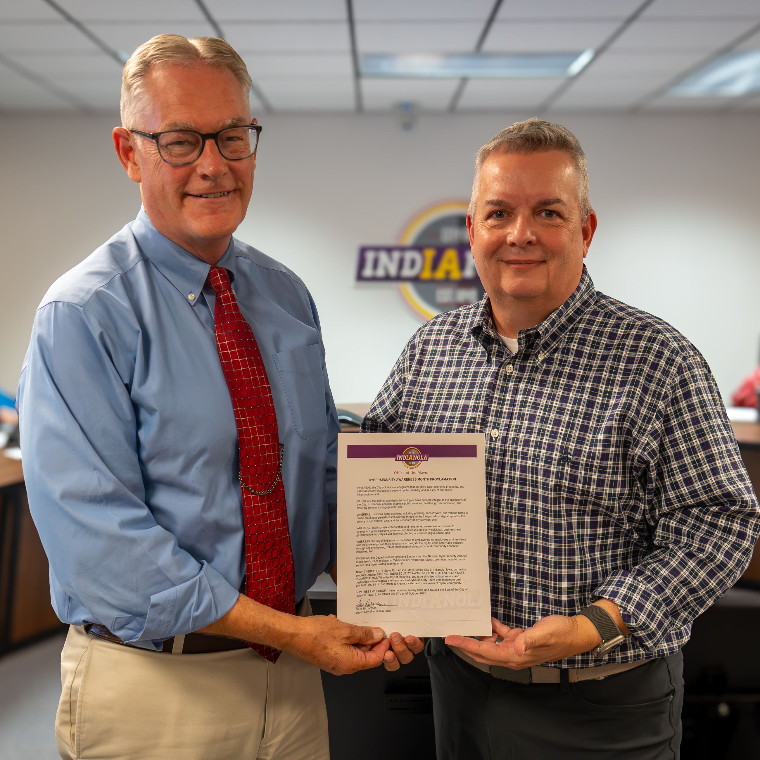 Two individuals hold a proclamation document during a meeting.