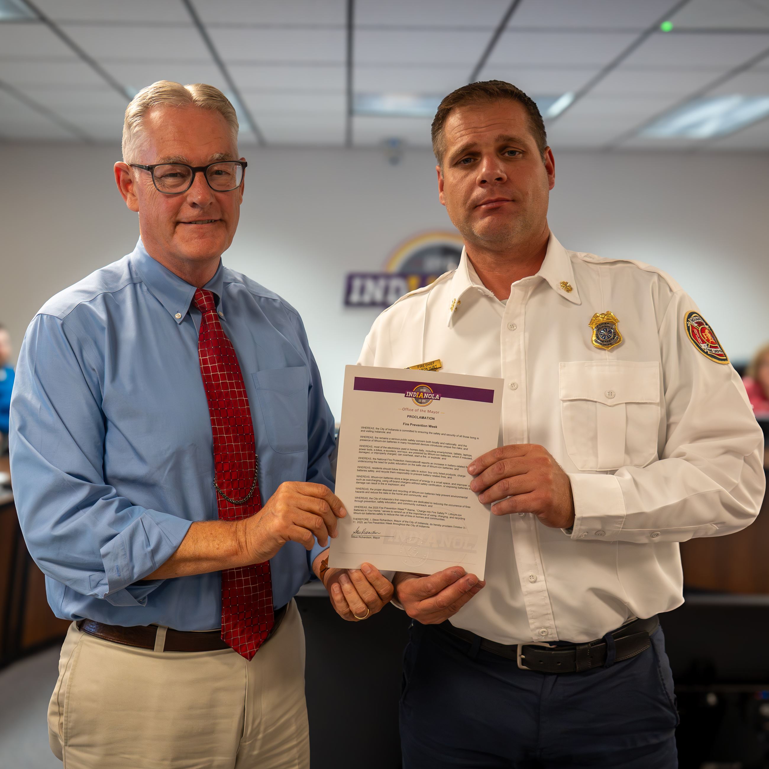 Two individuals hold a proclamation document during a meeting.