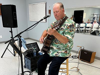Man sits on a stool and plays guitar and sings.