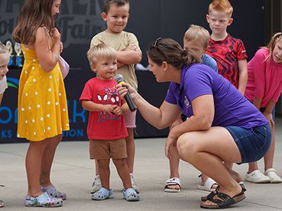 Small child speaks into a microphone during the rooster crowing contest, while other kids look on